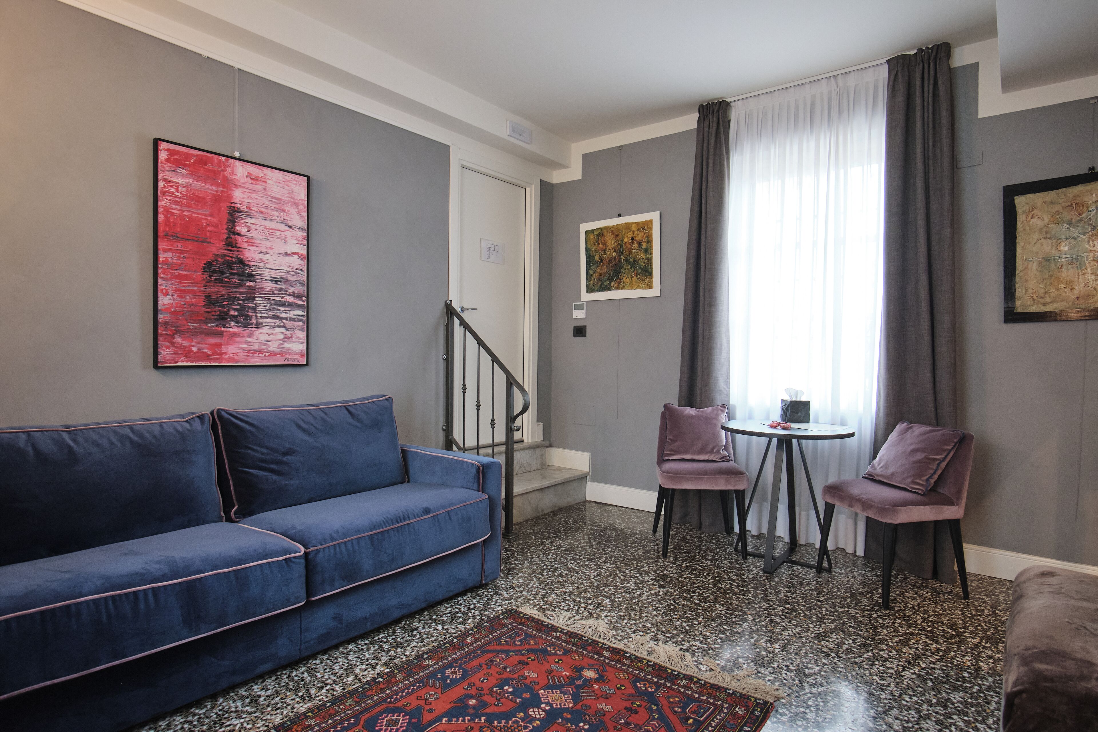 A modern living room with a blue sofa, two chairs, a small table, and a red patterned rug.