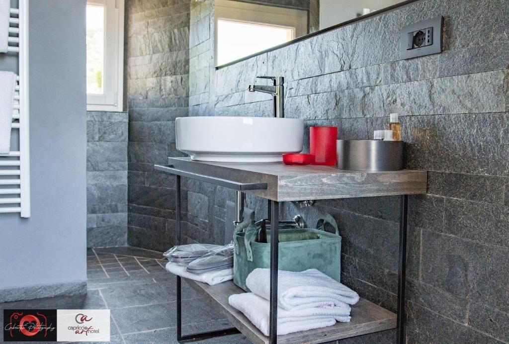 Ein modernes Badezimmer mit einem fest installierten weißen Waschbecken, einem Spiegel und einem Regal mit Handtüchern und Pflegeprodukten.