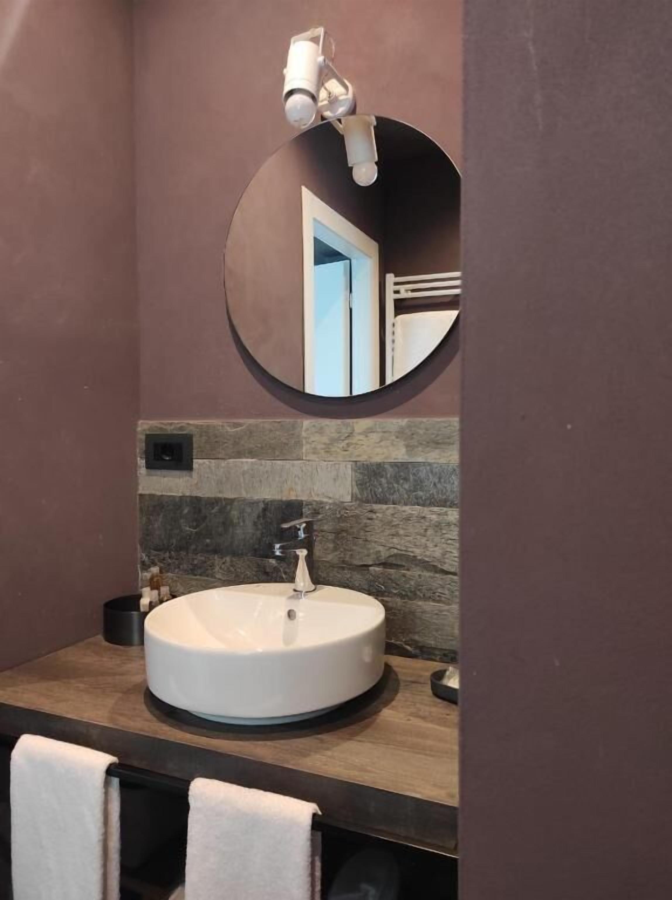 A bathroom with a round mirror, a white sink, and a towel rack.