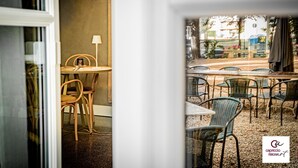 Un espacio interior con asientos de madera, mesas, una lámpara y vistas del patio exterior con sillas y mesas de mimbre.