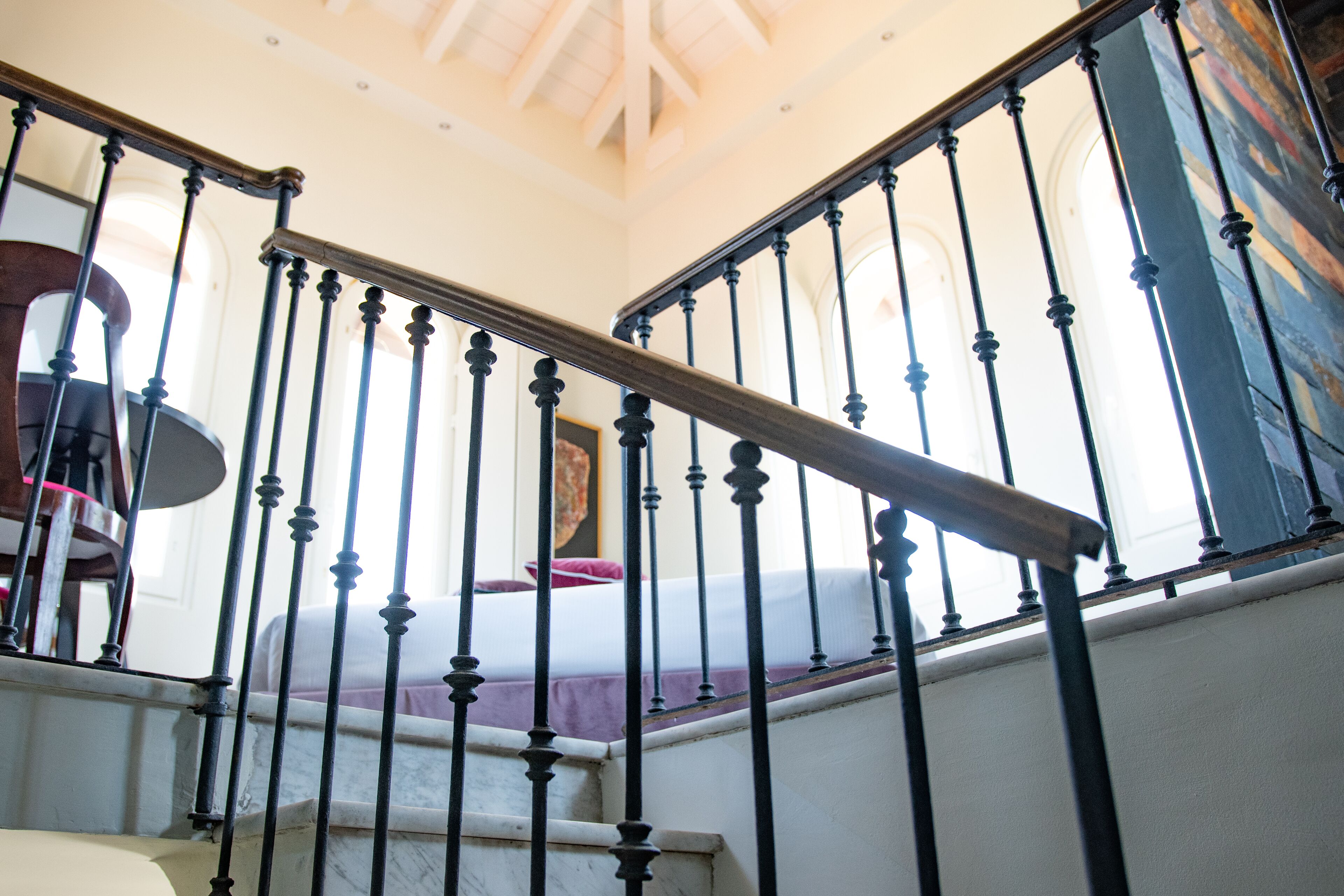 A staircase with a wooden handrail and black balusters, leading to a room with a bed and a painting on the wall.