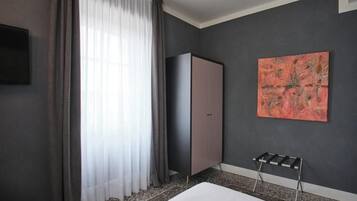 A modern hotel room with a large bed, a wardrobe, a painting on the wall, and a window with curtains.