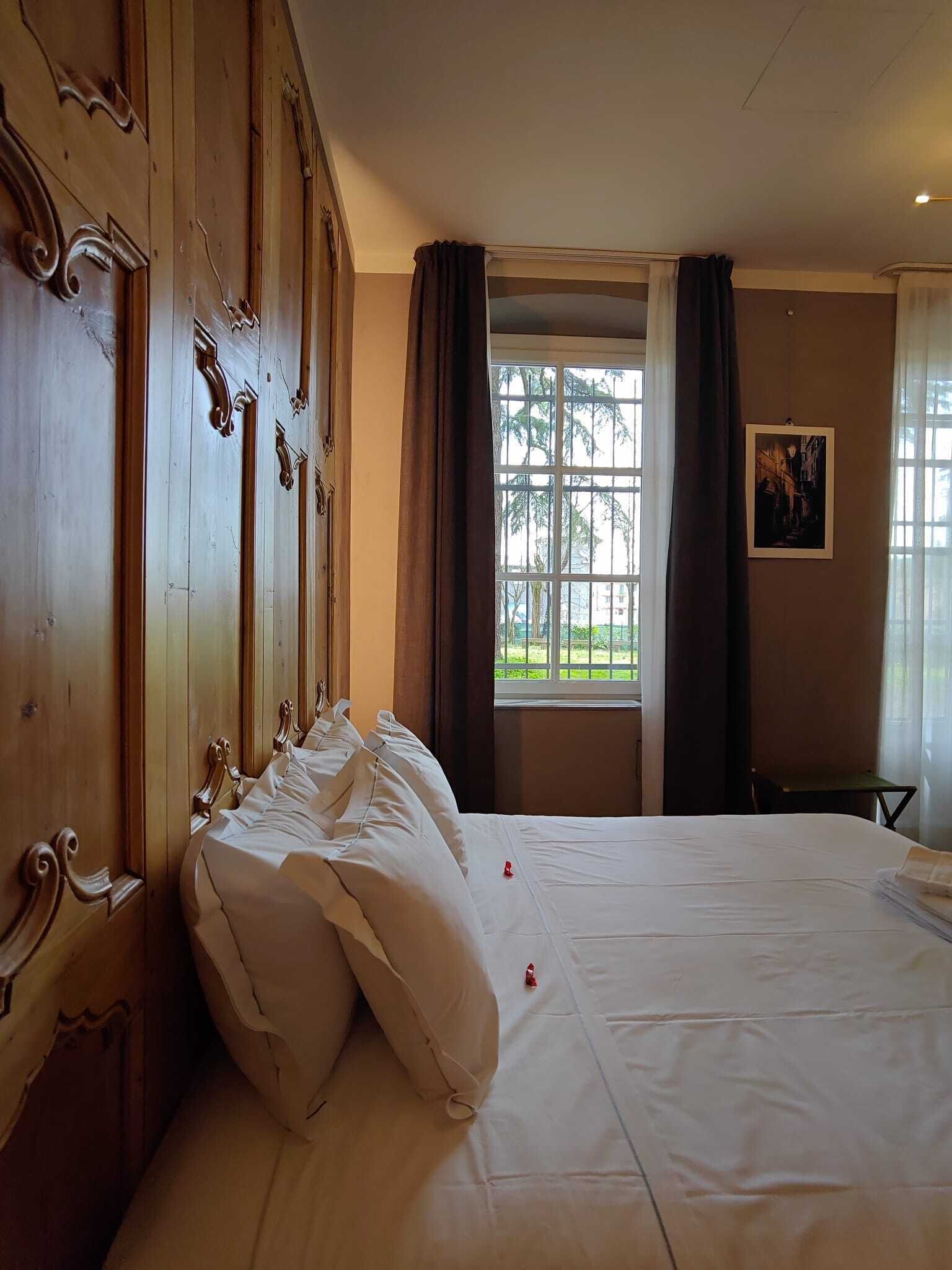 Ein Hotelzimmer mit einem großen Bett, einem Holzschrank, einem Fenster mit Vorhängen und einem gerahmten Bild an der Wand.