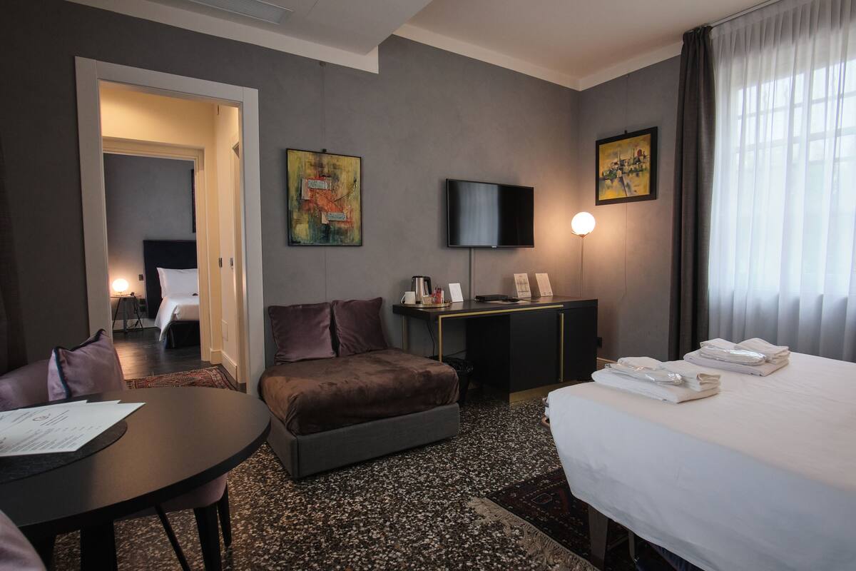 Ein Hotelzimmer mit Bett, Schreibtisch, Stuhl, Sofa, Fernseher und Bildern an den Wänden.