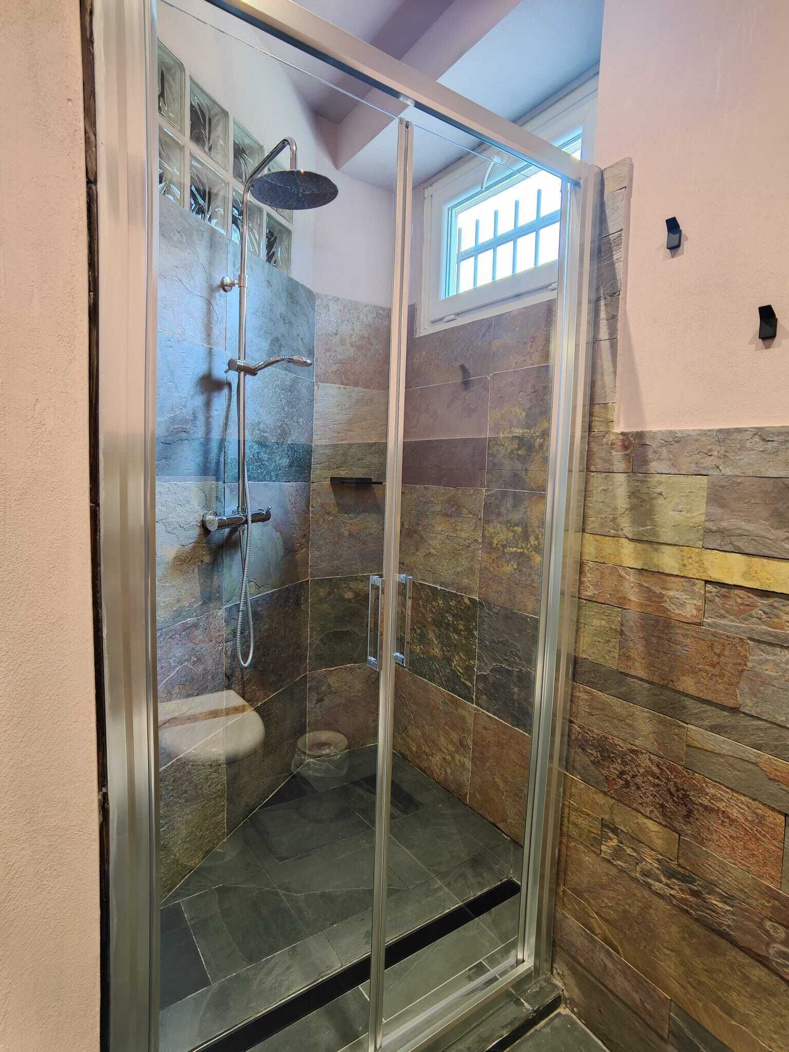 A glass-enclosed shower with a stone wall backdrop, a window, and a visible showerhead.