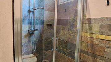 A glass-enclosed shower with a stone wall backdrop, a window, and a visible showerhead.