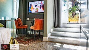 Habitación de hotel con televisión, dos sillones, cama, escritorio y vista a un árbol.