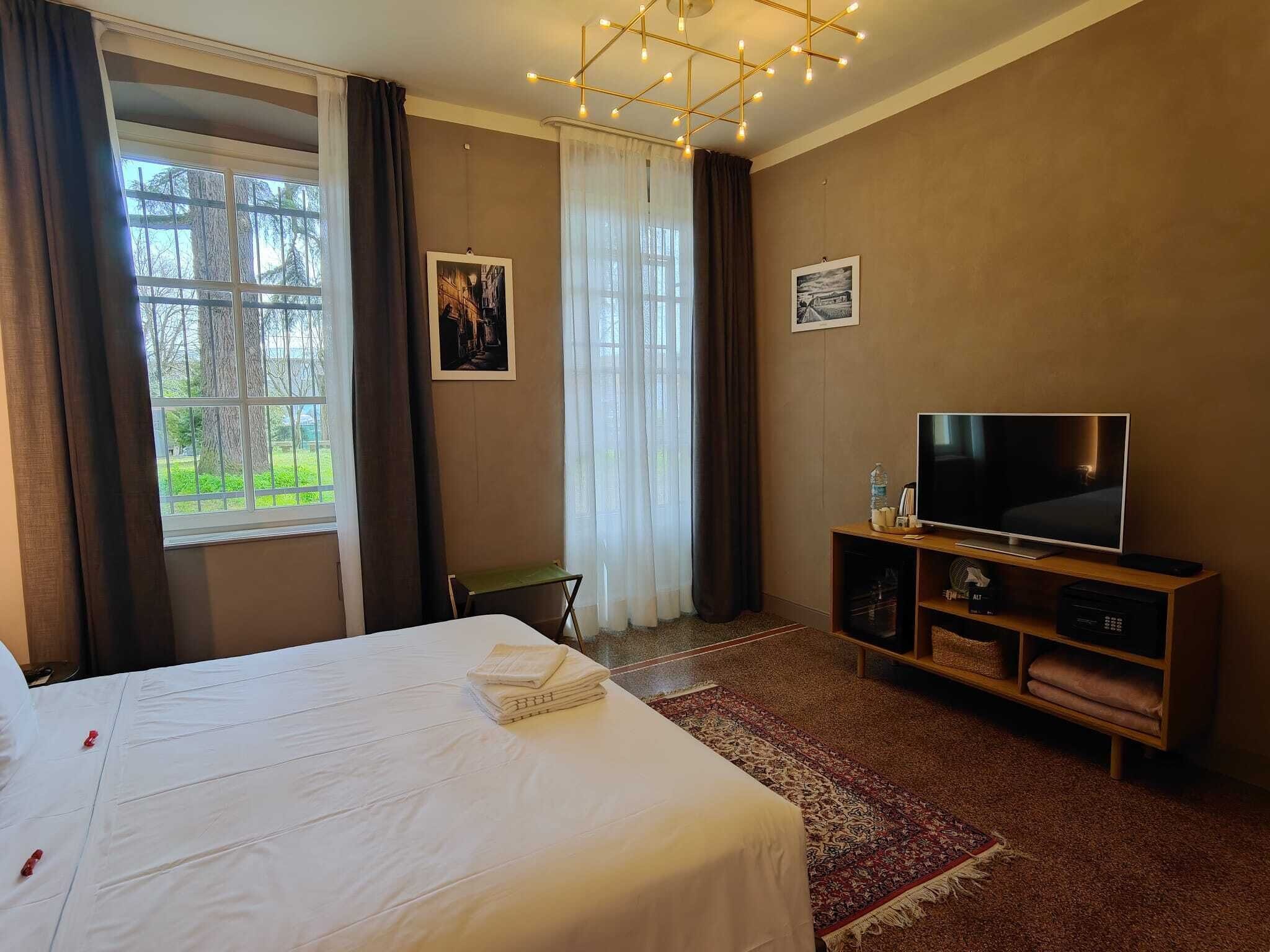 A hotel room with a bed, a TV, a small table, and a window with curtains.