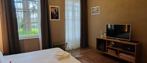 A hotel room with a bed, a TV, a small table, and a window with curtains.