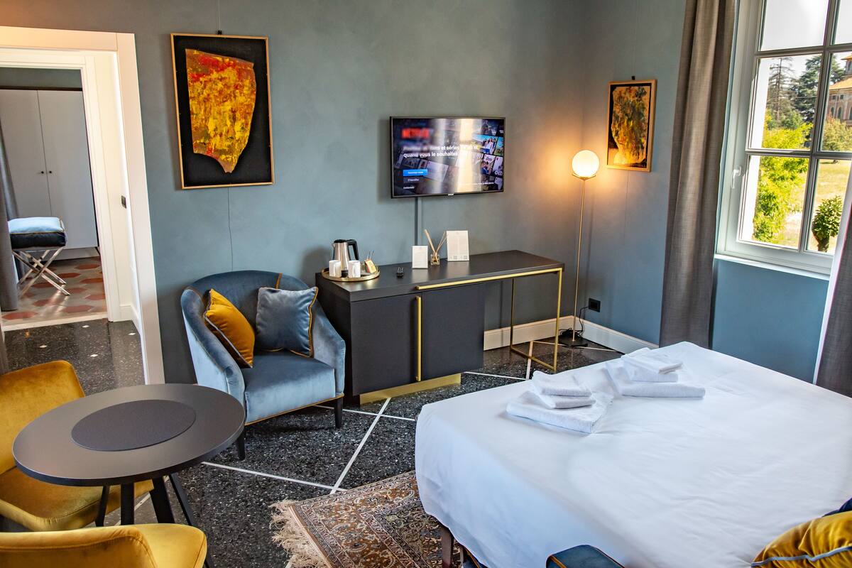 Ein Hotelzimmer mit einem Bett, einem Schreibtisch, einem Sessel, einem Fernseher und Kunstwerken an den Wänden.
