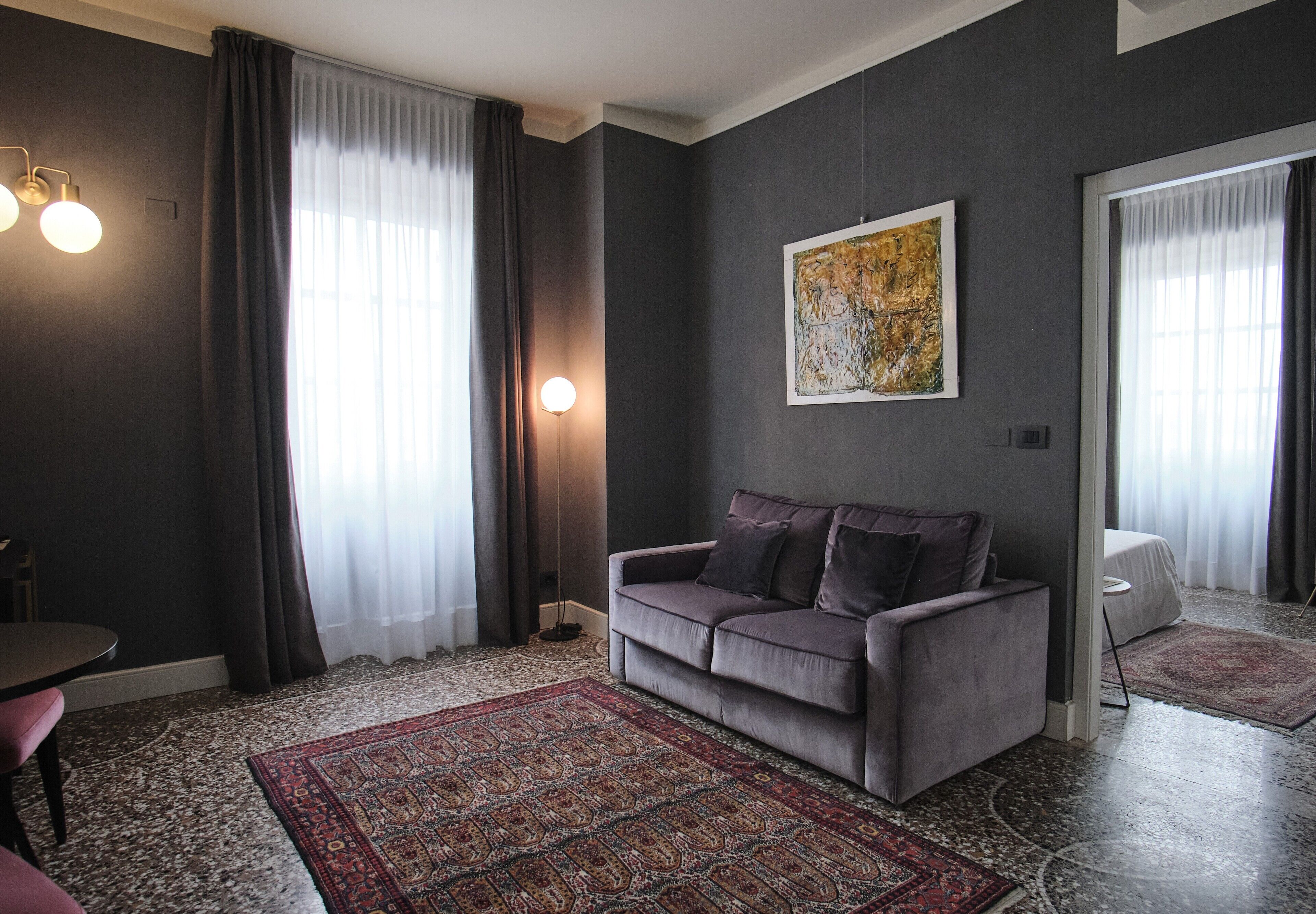 A modern living room with a grey sofa, a patterned rug, and a large abstract painting on the wall.