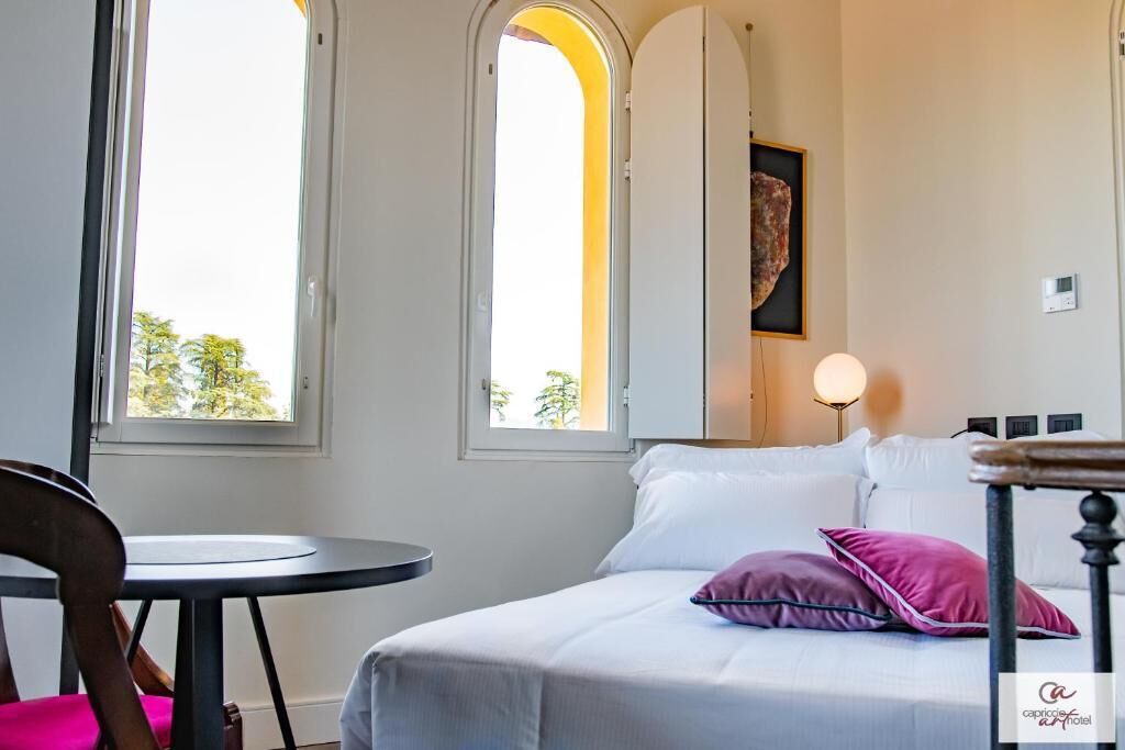 Una habitación de hotel con una cama, una mesa redonda y dos ventanas.