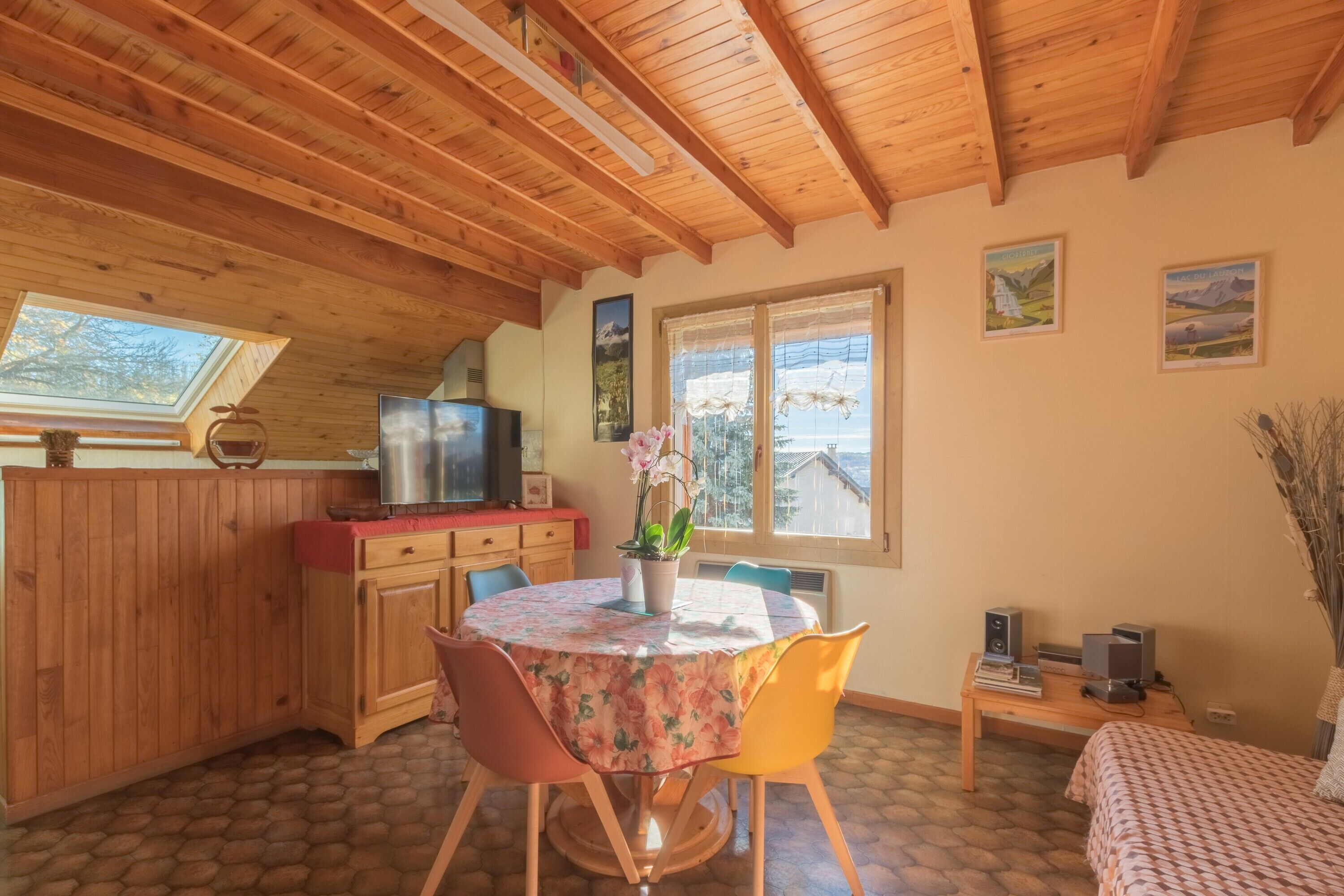 Eine gemütliche Küche mit Holzbalken, einem Esstisch mit Stühlen, einem Fenster mit Aussicht und einem kleinen Tisch mit elektronischen Geräten.