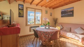 Une pièce chaleureuse avec un plafond en bois, une table à manger avec des chaises, un canapé et une fenêtre donnant sur un beau paysage.