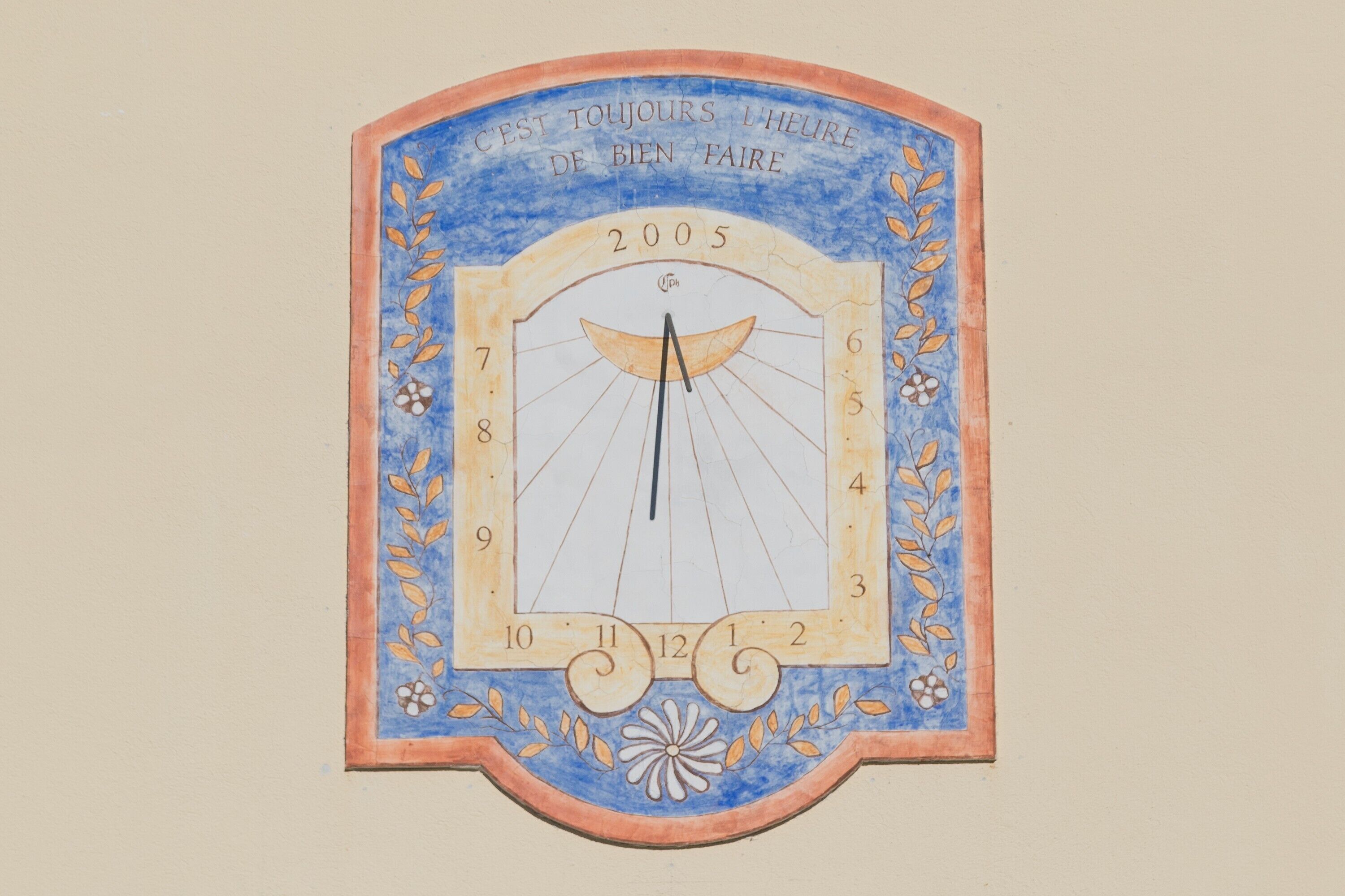 A wall-mounted clock with a decorative frame and the inscription 'C'est toujours l'heure de bien faire' and the year '2005'.