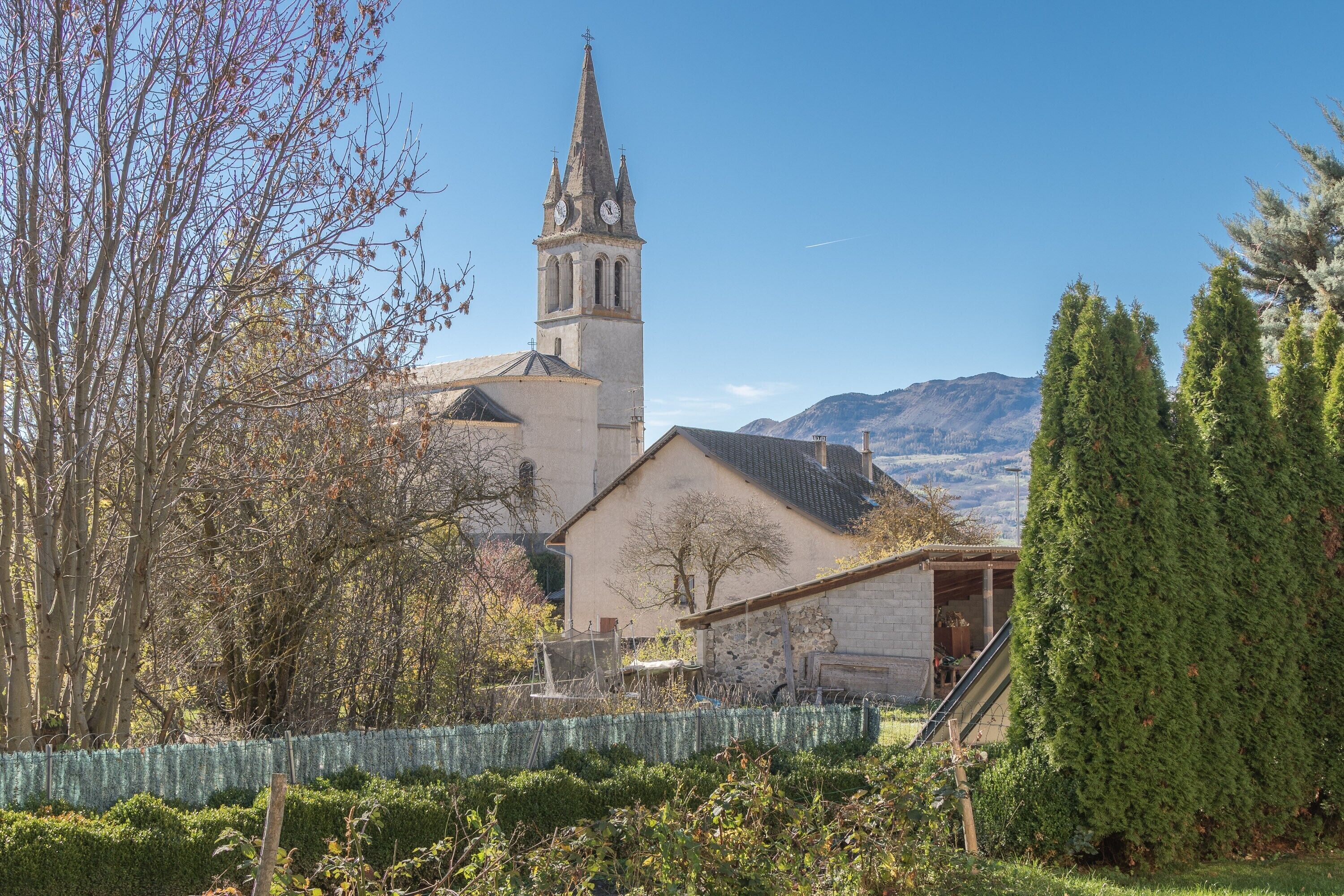 Eine Kirche mit Kirchturm, ein kleines Nebengebäude und ein eingezäunter Gartenbereich.