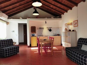 Un salón acogedor con una mesa de comedor, dos sofás, una zona de cocina con fregadero y hornalla, y un techo alto con vigas a la vista.