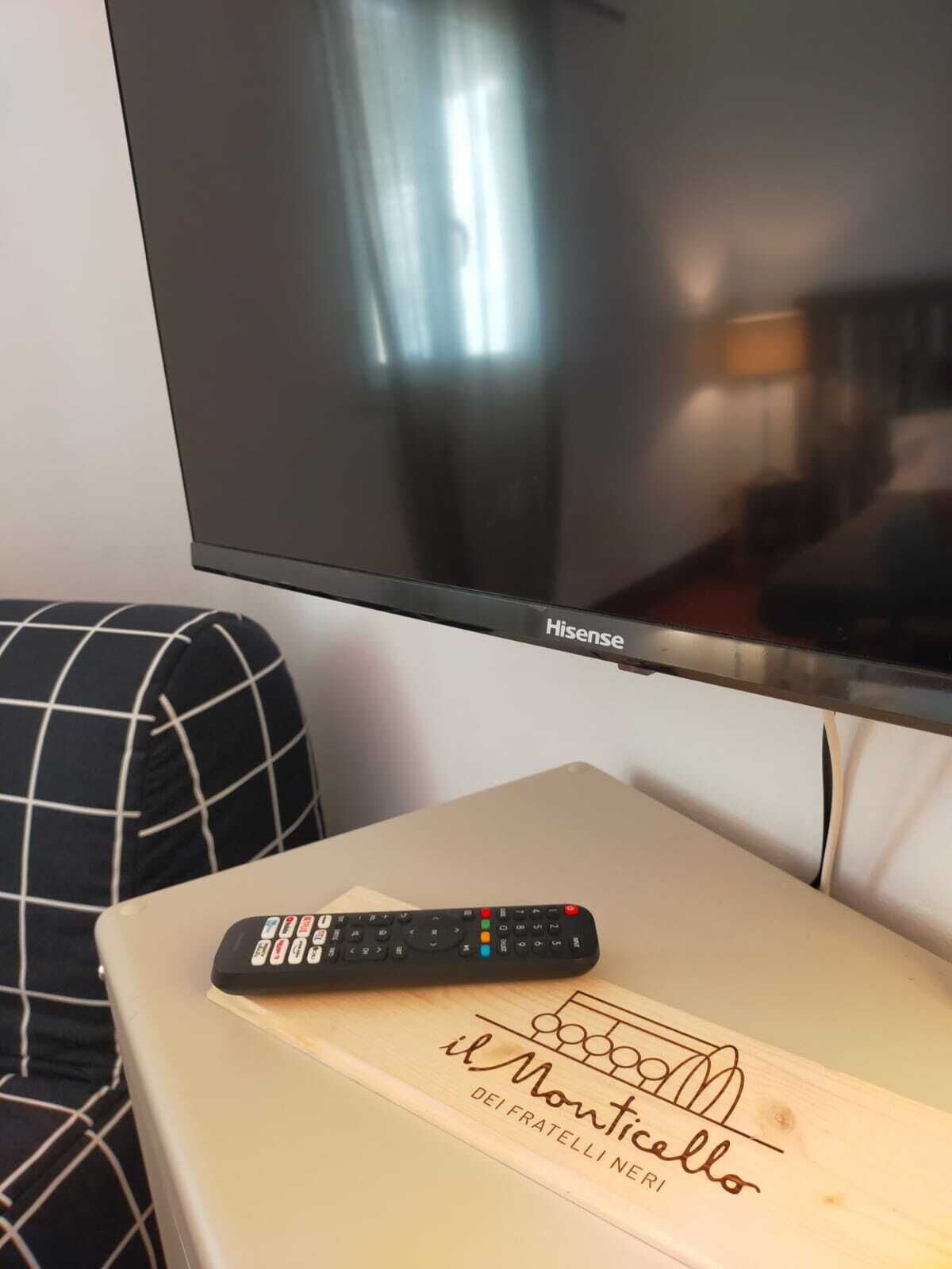 Un televisor de pantalla plana montado en una pared, un control remoto sobre una mesa de madera y un sofá con estampado blanco y negro.