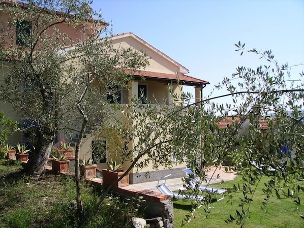 A two-story house with a red-tiled roof, a balcony, and a small swimming pool.