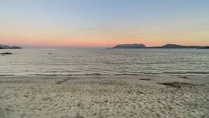Une plage avec une mer calme, un rivage sablonneux et des montagnes à l’horizon.