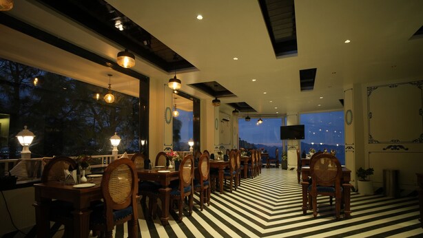 A dining area with a black and white striped floor, wooden chairs, and pendant lighting. - Oakhill Resort (Kasauli)