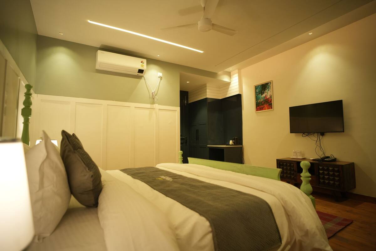 A bedroom with a bed, a TV, an air conditioner, and a ceiling fan.