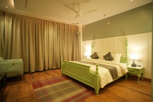 Una camera da letto con un letto verde, un comodino con una lampada, una sedia e una finestra con tende.