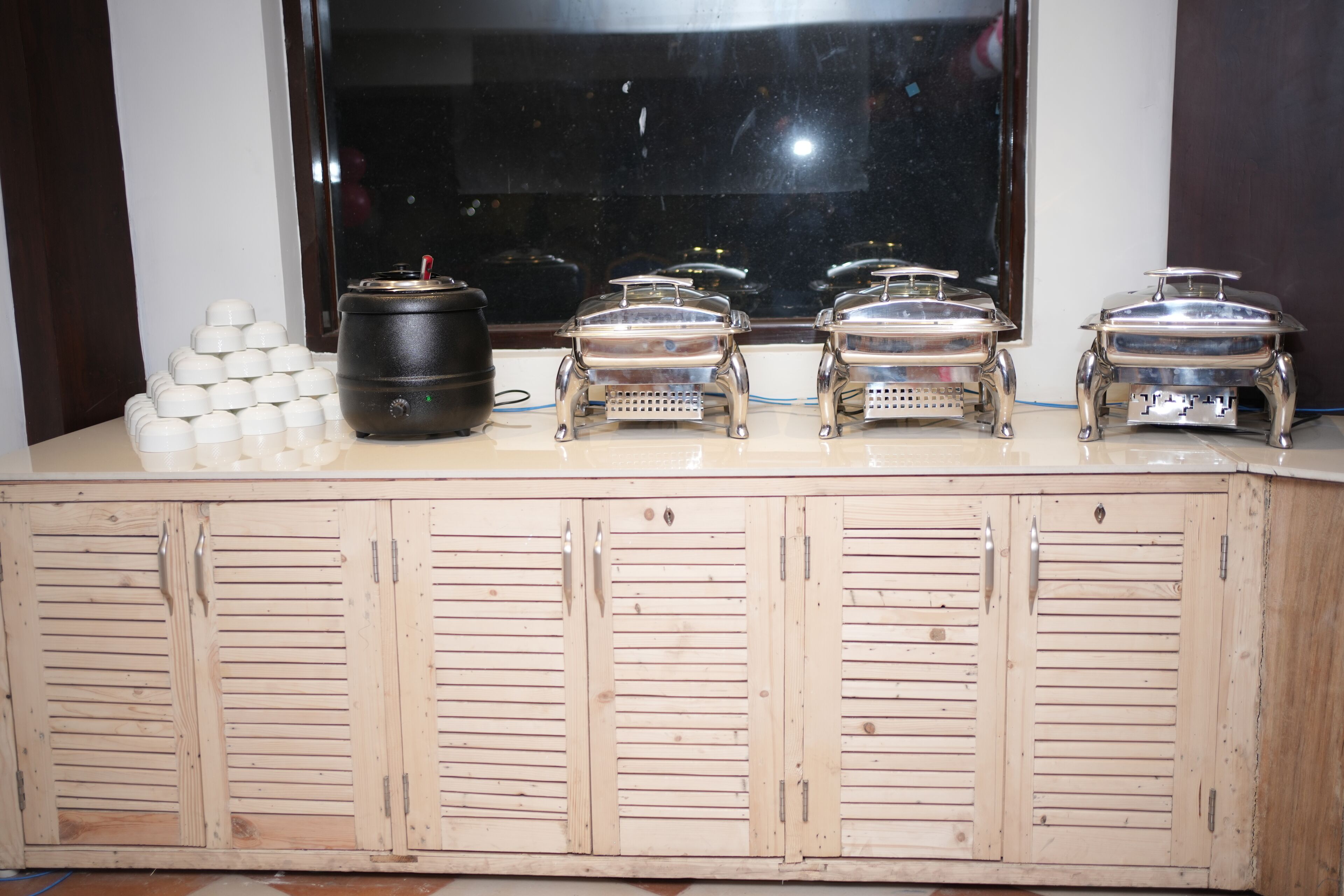 A buffet setup with multiple serving stations and a large window in the background.