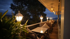 An outdoor seating area with wicker furniture and white tables, illuminated by hanging lanterns. - Oakhill Resort (Kasauli)
