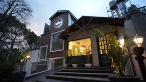 A modern hotel entrance with a wooden facade, large windows, and a red carpet leading to the door. - Oakhill Resort (Kasauli)