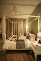 Una cama con dosel, ropa de cama blanca y pétalos de rosa.