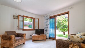 Ein Wohnzimmer mit Rattanmöbeln, einem Flachbildfernseher und einer Schiebetür zum Garten.