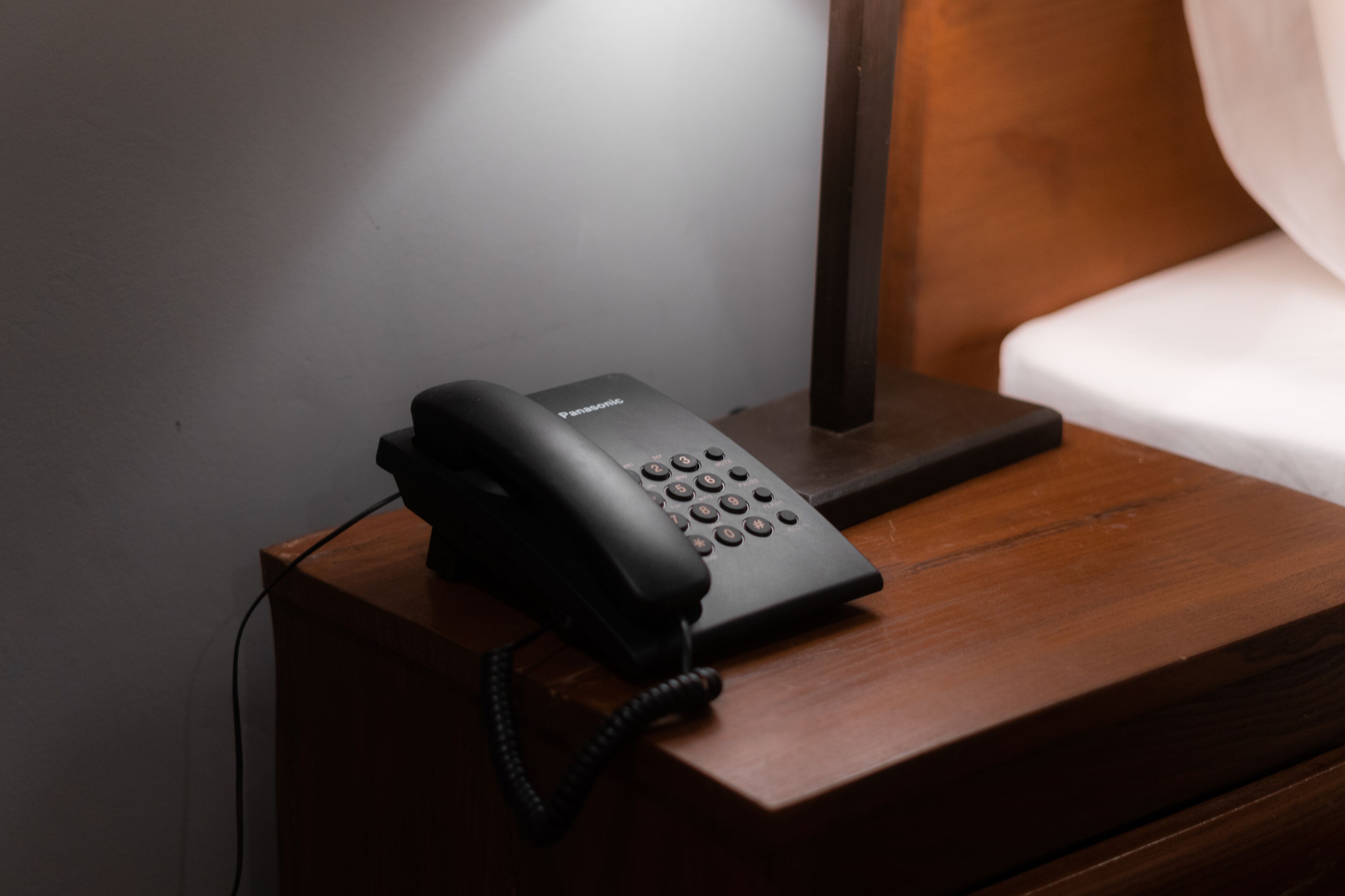 Un teléfono negro sobre una mesita de noche de madera, junto a una lámpara.