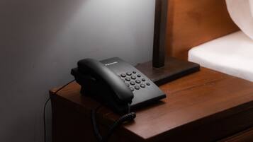 Un teléfono negro sobre una mesita de noche de madera, junto a una lámpara.