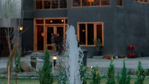 Un bâtiment moderne doté d’une grande entrée vitrée, d’une fontaine en premier plan et d’un jardin bien entretenu.