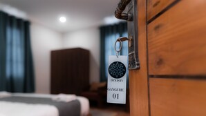 Une chambre d’hôtel avec une armoire en bois, un lit recouvert d’une couette grise et blanche, et une pancarte indiquant le numéro de chambre : 01.