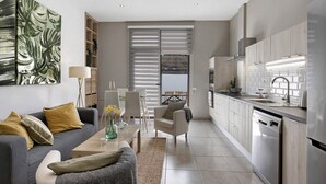 Eine moderne Küche mit Geschirrspüler, eine Essecke mit Tisch und Stühlen sowie ein Wohnzimmer mit Sofa und Lampe.