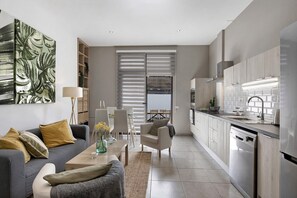 A modern kitchen with a dishwasher, a dining area with a table and chairs, and a living room with a sofa and a lamp.