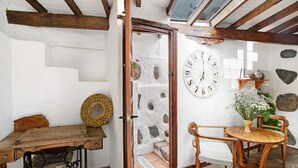 A rustic room with a wooden table, a sewing machine, a wooden chair, a large wall clock, and stone walls. - Vacation Home "La Casa Nueva" with Mountain View, Whirlpool & Wi-Fi (Fataga)
