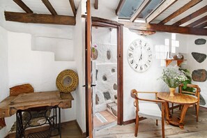 Une pièce rustique avec une table en bois, une machine à coudre, une chaise en bois, une grande horloge murale et des murs en pierre.