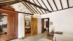 A bedroom with a wooden wardrobe, a bed with a patterned bedspread, a small table with a lamp, and a wooden ceiling with exposed beams. - Vacation Home "La Casa Nueva" with Mountain View, Whirlpool & Wi-Fi (Fataga)