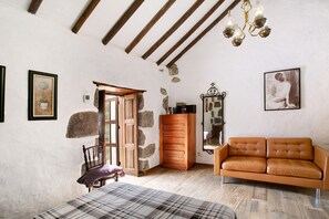 A room with a wooden ceiling, a brown leather sofa, a plaid bedspread, and stone walls.