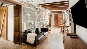 A room with a stone wall, a leather sofa, wooden furniture, and a television. - Vacation Home "La Casa Nueva" with Mountain View, Whirlpool & Wi-Fi (Fataga)