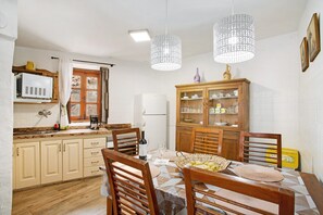 A kitchen with wooden cabinets, a dining table with chairs, a refrigerator, and hanging pendant lights.