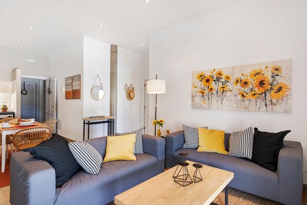 Un salon avec deux canapés, une table basse et un tableau représentant des tournesols.