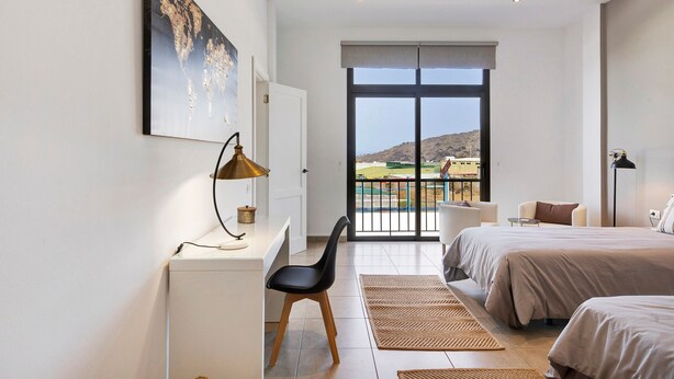 Un dormitorio con cama, escritorio, silla, ventana grande y vista al paisaje.