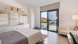 Un dormitorio con cama, armario, silla, lámpara y balcón con vistas.