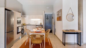 Una cocina moderna con electrodomésticos de acero inoxidable, un comedor con sillas de mimbre y una pequeña mesa con libros.