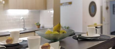 A kitchen counter with a bowl of fruit, a muffin, and two cups.