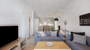 A modern living room with a flat-screen TV, a sofa, a coffee table, and a dining area in the background.